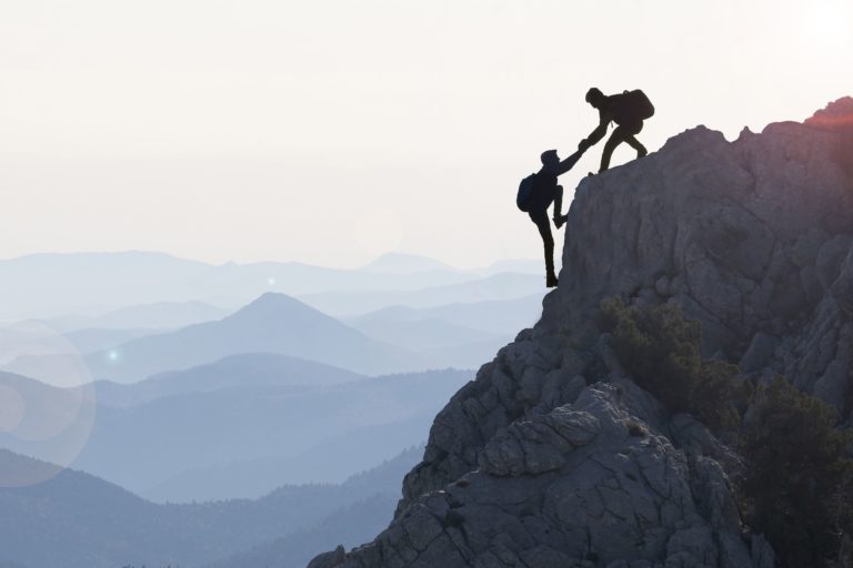 Ein Bergsteiger hilft seinem Freund bis auf die Spitze - LuArtX unterstuetzt Sie bis zum Erfolg
